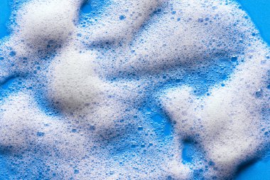 Yüz temizleyici köpük örneği. Mavi arka planda beyaz köpük köpüğü. Sabun, duş jeli, şampuan köpüğü dokusu yakından..