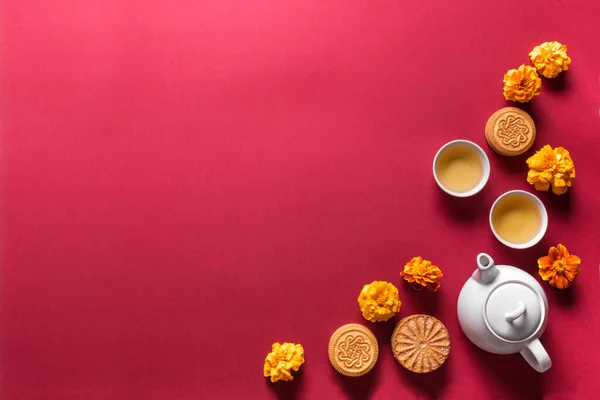 Mid Autumn festival concept. Chinese moon cake, tea and flowers on red background, top view, copy space.