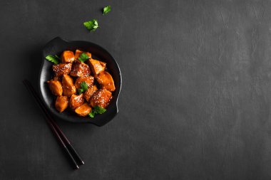 Teriyaki tavuk parçaları susamlı ve siyah arka planda yeşillikler, kopyalama alanı. Asya usulü yemek. Teriyaki soslu kızarmış tavuk filetosu..