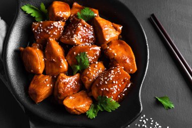 Teriyaki tavuk parçaları susamlı ve siyah arka planda yeşillikler yakın plan. Asya usulü yemek. Teriyaki soslu kızarmış tavuk filetosu..