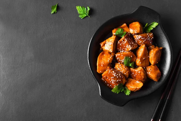 Teriyaki tavuk parçaları susamlı ve siyah arka planda yeşillikler, kopyalama alanı. Asya usulü yemek. Teriyaki soslu kızarmış tavuk filetosu..