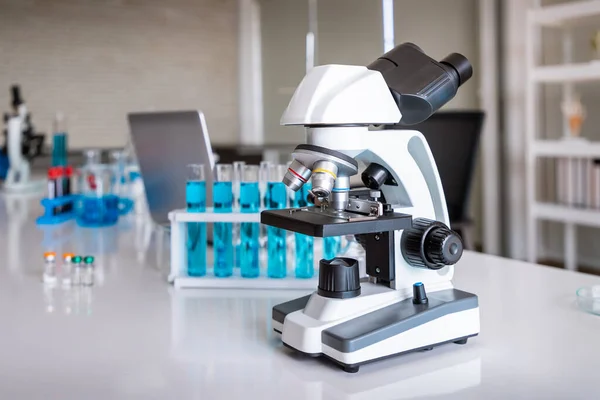 Microscope examining slide of sample with test tubes in background. Concept for science and technology research in laboratory.