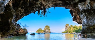 Krabi, Thailand - February 16, 2020: Majestic cave and limestone cliff mountain at Phra Nang Beach, famous tourists destination. clipart