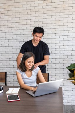 Asyalı koca, evde çalışan, oturma odasında masa başında yemek yiyen bir kadını destekliyor.