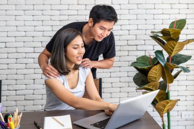 Asyalı koca, evde çalışan, oturma odasında masa başında yemek yiyen bir kadını destekliyor.