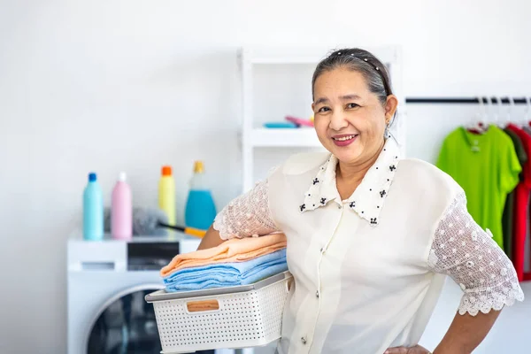 洗濯機と洗濯機 掃除や家事をし カメラを見て バスケットを運ぶ幸せな笑顔アジアの高齢女性高齢者の女性 ストック画像