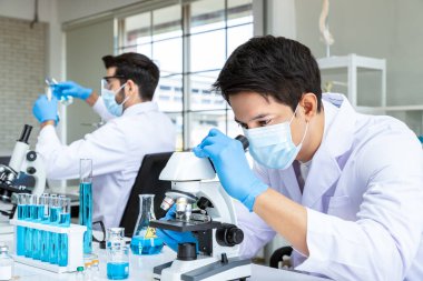 Laboratuvarda çalışan iki Asyalı ve Arap araştırmacı bilim adamı bilimsel ekipman ve mikroskop ile biyolojik tehlike maddesi üzerinde çalışıyorlar.