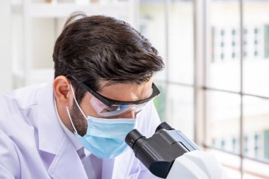 Yakın plan Arap erkek araştırmacı bilim adamı. Mikroskop altında cerrahi maske takan tıp doktoru.