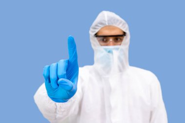 Dokunma düğmesi, Orta Doğulu Arap erkek araştırmacı tıp doktoru Kişisel Koruyucu Ekipman (PPE), cerrahi maske ve koruma gözlüğü takan, açık mavi arka planda duran