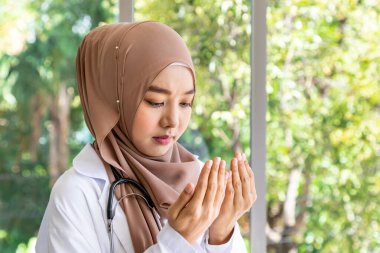 Kendine güvenen güzel Müslüman kadın doktor steteskopla ayakta durup dua ediyor.