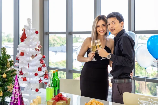 Attractive young couple celebrate Christmas and New Year in party, clinking champagne glass, with snack and beverage on table
