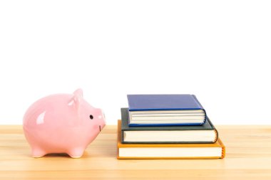 Tahta masadaki pembe kumbarada beyaz arka planda kitap yığını, eğitim ve burs için tasarruf kavramı