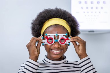 Afrikalı genç bir kız klinikte ya da optik dükkanda deneme aşamasında göz muayenesi yapıyor. Göz konsepti.