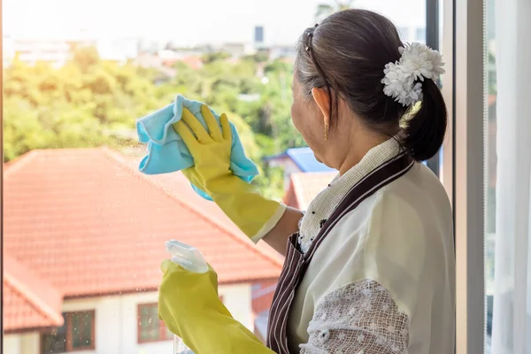 快乐的亚洲老年女性使用喷雾瓶和布来清洁玻璃窗 — 图库照片