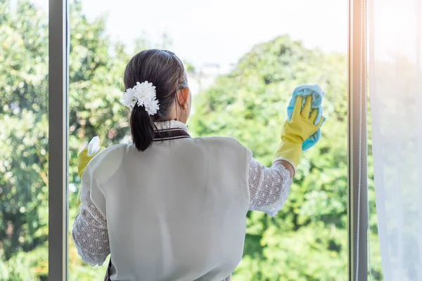 快乐的亚洲老年女性使用喷雾瓶和布来清洁玻璃窗 — 图库照片