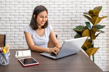 Evde çalışan, oturma odasındaki masa başında yemek yiyen Asyalı kadın portresi.