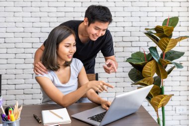 Asyalı koca, karısını motive etti. Kadın serbest çalışıyor, oturma odasında masa başında yemek yiyor.