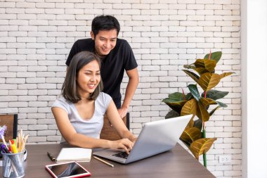 Asyalı koca, karısını motive etti. Kadın serbest çalışıyor, oturma odasında masa başında yemek yiyor.