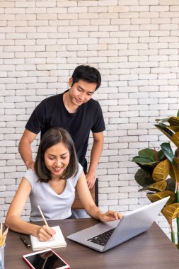 Asyalı koca, evde çalışan, oturma odasında masa başında yemek yiyen bir kadını destekliyor.