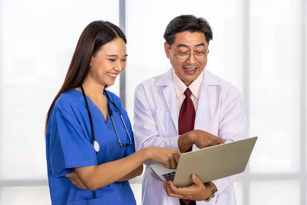 Happy Asian male and female medical doctor standing and discussing about case with laptop computer