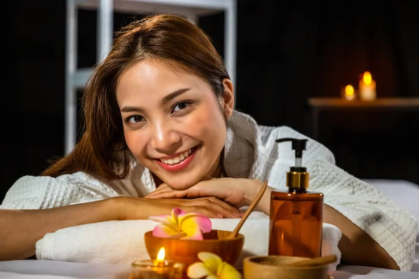 美丽的年轻亚洲女人躺在床上 躺在温泉里 用按摩油 洗涤剂和蜡烛 看着相机 — 图库照片