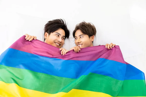 Mutlu Asyalı Homoseksüel Çift Beyaz Yatakta Yatarken Gökkuşağı Gurur Bayrağı - Stok İmaj