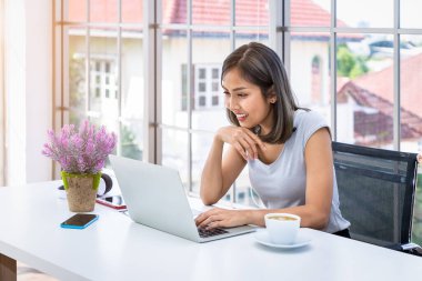 Evde çalışan, oturma odasındaki masa başında oturan Asyalı kadın portresi.