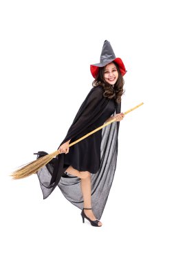 Siyah pelerinli cadı kostümü giymiş Asyalı bir kadın beyaz arka planda elinde süpürge sopasıyla kameraya bakıyor.