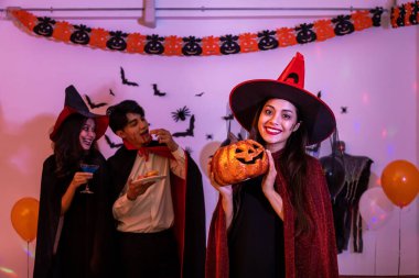 Cadılar Bayramı kostümünde gülümseyen genç Asyalı kadın portresi partideki cadı, balkabağı ya da Jack O Lantern gibi, kameraya bakıyor..