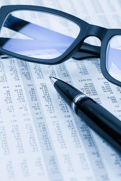 Penna och glasögon vila på aktiekursen detalj finansiell tidning — Stockfoto