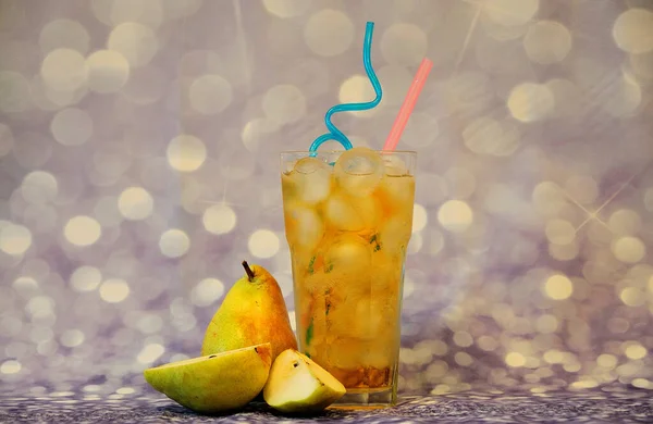 A glass of pear juice with ice and straws stands on a gray shiny background next to ripe fruits. Close-up.