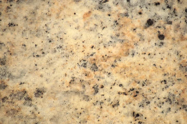 Pale yellow granite with small black inclusions. Background, pattern, texture.