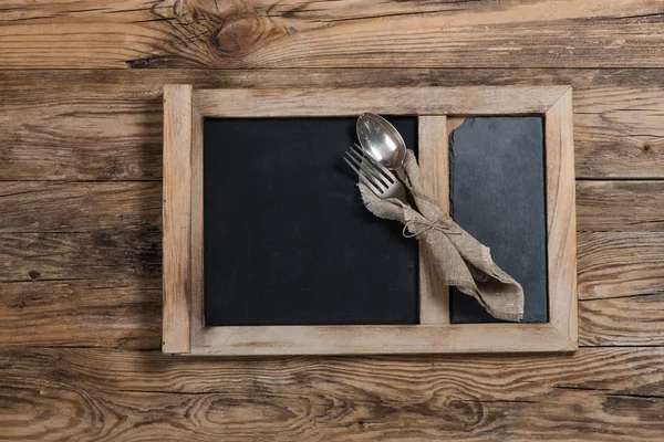 Dinnerware - fork and spoon in napkin on a chalkboard on wooden — Stock Photo, Image