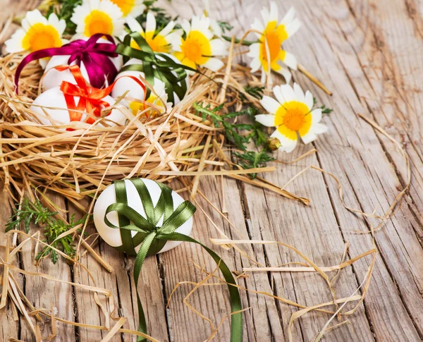 Easter eggs with color bows in a nest  and spring flowers — Stock Photo, Image