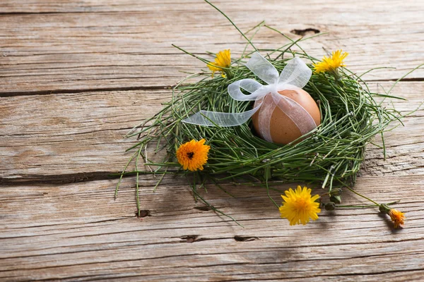 Close-up of egg with ribbon in a nest with flowers — Stock Photo, Image