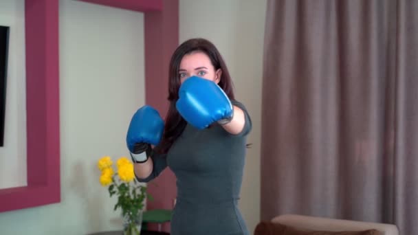 Młoda dziewczyna gospodyni domowa boks w domu w powietrzu z niebieskimi rękawicami bokserskimi w zwolnionym tempie. — Wideo stockowe