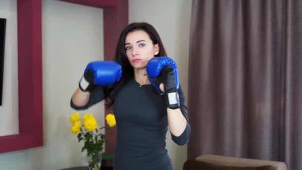 Jovem dona de casa boxe em casa no ar com luvas de boxe azul. 4k — Vídeo de Stock