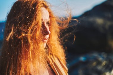 Kızıl saçlı bir kızın portresi denizin arka planında rüzgârda gelişiyor..