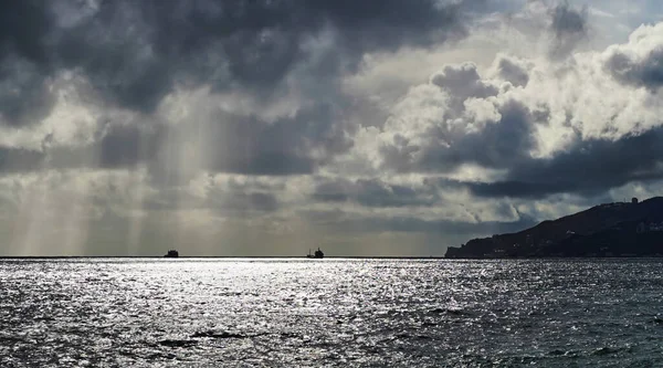 The landscape of the sea in cloudy weather, the sun shines through the clouds, tankers are drifting in the sea.
