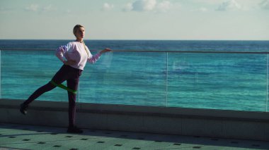 Genç bir kız güneşli bir günde sabah egzersizi yapar. Genç sarışın spor için denizin arka planına gider..