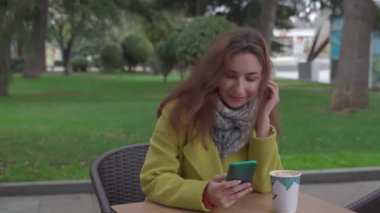 Kışın açık bir kafede genç bir Ermeni kız sıcak kahve içiyor ve akıllı bir telefonla görüntülü sohbet yapıyor, gülüyor ve hava öpücüğü gönderiyor..