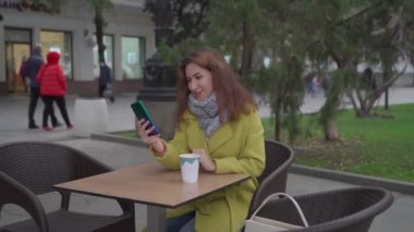 Kışın açık bir kafede genç bir Ermeni kız sıcak kahve içiyor ve akıllı bir telefonla görüntülü sohbet yapıyor, gülüyor ve hava öpücüğü gönderiyor..