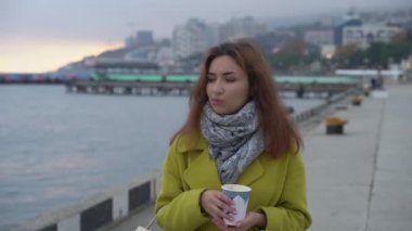 Genç Ermeni bir kızın portresi denizin arka planında kıyıda yürüyor ve kışın sıcak kahve içiyor..