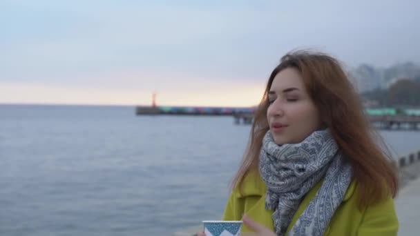 Портрет молодой армянской девушки крупным планом на фоне моря, идущей вдоль берега и пьющей горячий кофе зимой. — стоковое видео