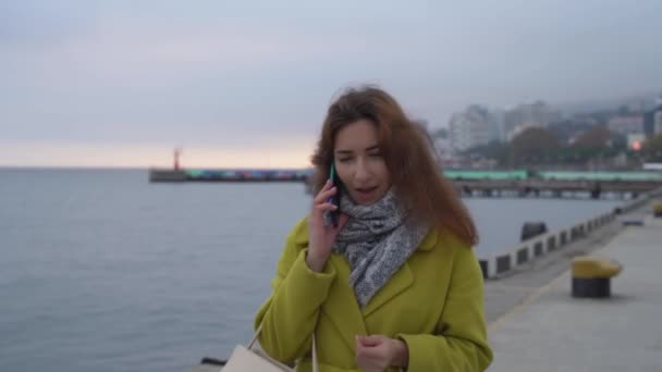 Portrait d'une jeune Arménienne en gros plan sur fond de mer marchant dans la ville et parlant sur un téléphone portable souriant et riant. — Video