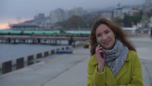 Portræt af en ung armensk pige close-up på baggrund af havet gå i byen og taler på en mobiltelefon smilende og griner. – Stock-video