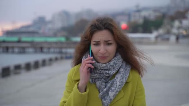 Portretul unei tinere fete armene de aproape pe fundalul mării mergând în oraș și vorbind indignat pe un telefon mobil, argumentează și nemulțumit — Videoclip de stoc