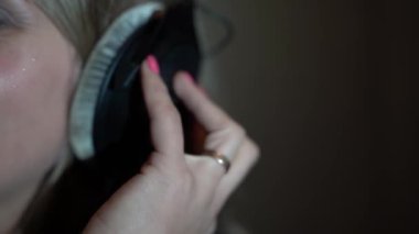 Küçük bir kayıt stüdyosundaki bir kadın stüdyo mikrofonunun önünde siyah kulaklık takarak mikrofona şarkı söylüyor. Bir kadın kayıt stüdyosunda şarkı söylüyor..