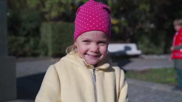 Ritratto ravvicinato di una bambina per strada in inverno, la ragazza agita la mano e sorride. — Video Stock