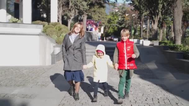 幸せな家族だ。母親と彼女の子供たちは手を握っていると女の子はお母さんと弟の間でジャンプしています. — ストック動画